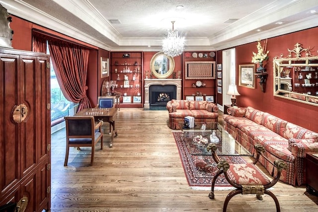 living room with a textured ceiling, a raised ceiling, crown molding, wood-type flooring, and an inviting chandelier