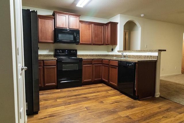 kitchen with kitchen peninsula, sink, light hardwood / wood-style floors, and black appliances