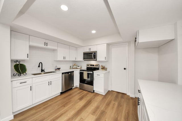 kitchen with sink, light hardwood / wood-style flooring, backsplash, white cabinets, and appliances with stainless steel finishes