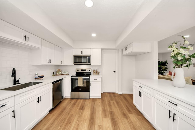 kitchen featuring backsplash, white cabinets, sink, light wood-type flooring, and appliances with stainless steel finishes