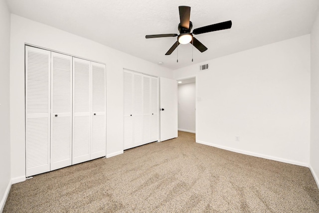 unfurnished bedroom featuring multiple closets, ceiling fan, and carpet