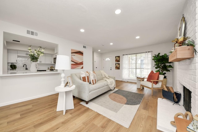 living room with sink, light wood-type flooring, and a brick fireplace