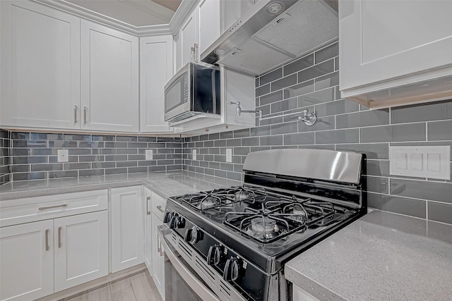 kitchen with light stone counters, wall chimney exhaust hood, stainless steel appliances, tasteful backsplash, and white cabinetry