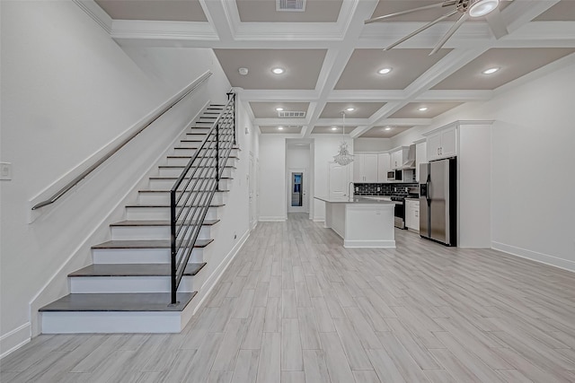 kitchen with appliances with stainless steel finishes, white cabinets, light hardwood / wood-style flooring, a kitchen island, and beam ceiling