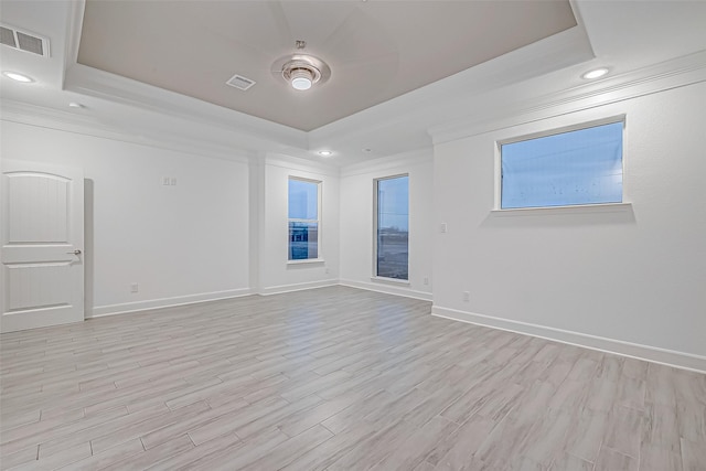 empty room with a raised ceiling, crown molding, and light hardwood / wood-style flooring