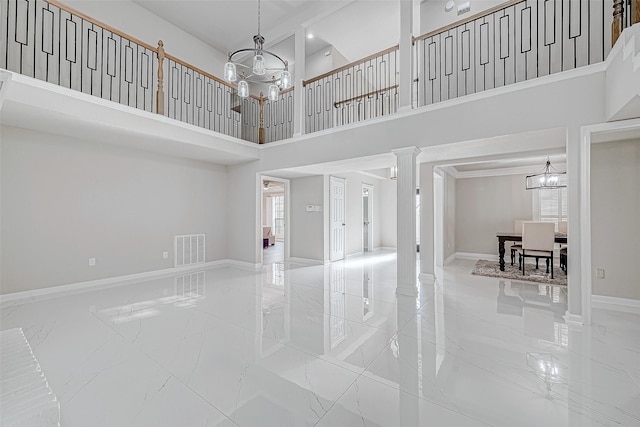 unfurnished living room with a high ceiling, decorative columns, a notable chandelier, and a healthy amount of sunlight