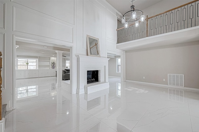 unfurnished living room featuring a fireplace, a chandelier, and ornate columns