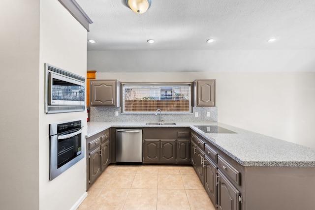 kitchen featuring kitchen peninsula, decorative backsplash, stainless steel appliances, sink, and light tile patterned floors