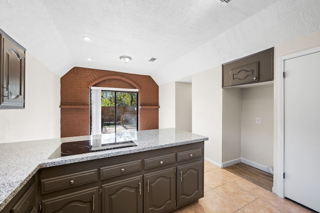 kitchen with a textured ceiling, vaulted ceiling, dark brown cabinets, light tile patterned flooring, and electric stovetop