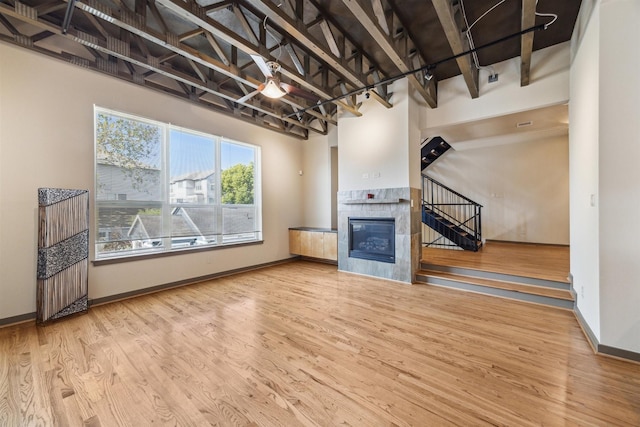 unfurnished living room with ceiling fan, wood-type flooring, a fireplace, and a towering ceiling