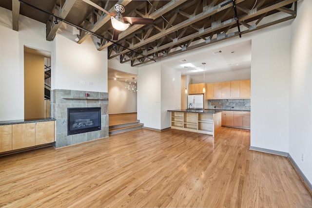 unfurnished living room with light hardwood / wood-style flooring, a towering ceiling, rail lighting, and a tiled fireplace