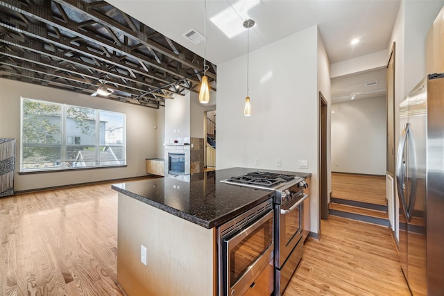 kitchen featuring decorative light fixtures, stainless steel appliances, dark stone counters, and light hardwood / wood-style flooring