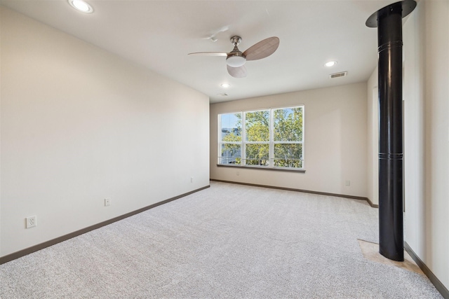 carpeted spare room with a wood stove and ceiling fan