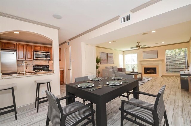 dining room featuring ceiling fan, ornamental molding, sink, and light hardwood / wood-style flooring