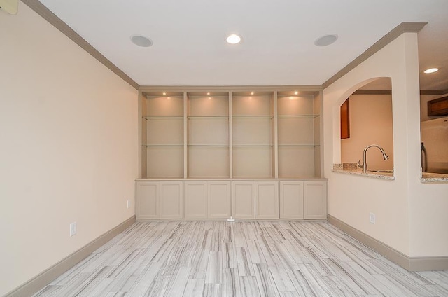 unfurnished room with built in shelves, sink, light hardwood / wood-style floors, and ornamental molding