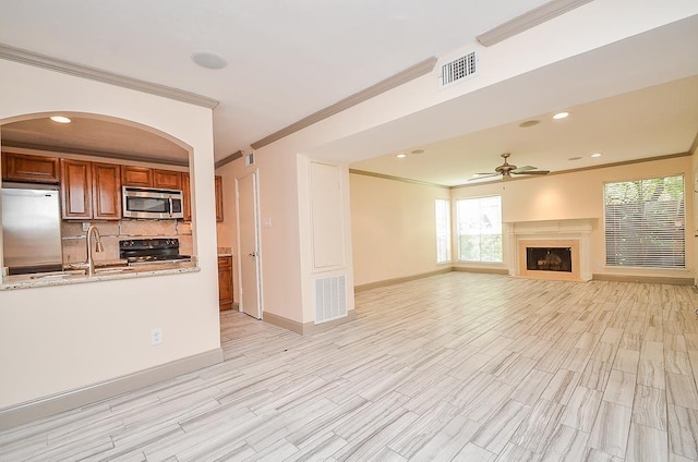 unfurnished living room with light wood-type flooring, ceiling fan, crown molding, and sink