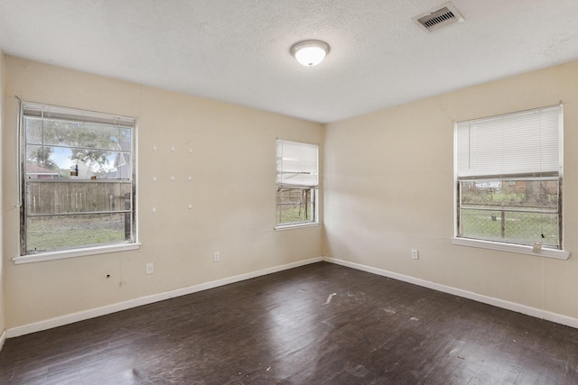 spare room featuring a textured ceiling, a healthy amount of sunlight, and dark hardwood / wood-style floors