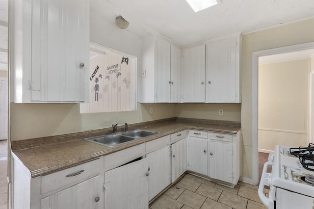 kitchen with white gas stove, white cabinetry, sink, and light tile patterned floors