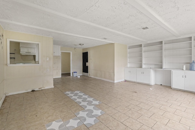 unfurnished living room with built in shelves, a textured ceiling, and light tile patterned floors