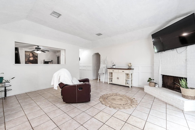 living room with a brick fireplace, ceiling fan, and light tile patterned flooring