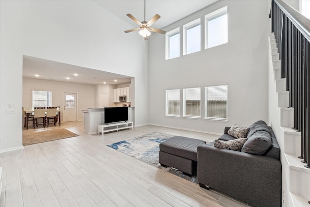 living room featuring a high ceiling, light hardwood / wood-style flooring, and ceiling fan