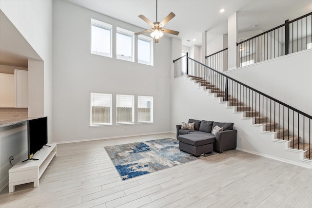 living room with ceiling fan, light hardwood / wood-style flooring, and a towering ceiling