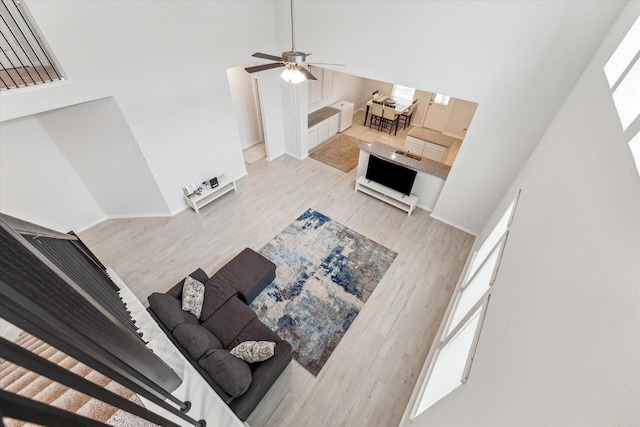 living room featuring ceiling fan, a towering ceiling, and light hardwood / wood-style flooring