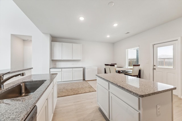 kitchen featuring white cabinets, a kitchen island, light stone countertops, and sink