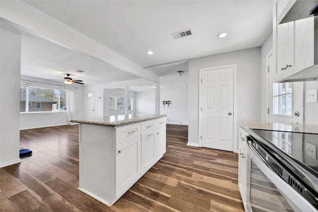 kitchen with stainless steel range with electric stovetop, white cabinets, ceiling fan, a kitchen island, and light stone counters