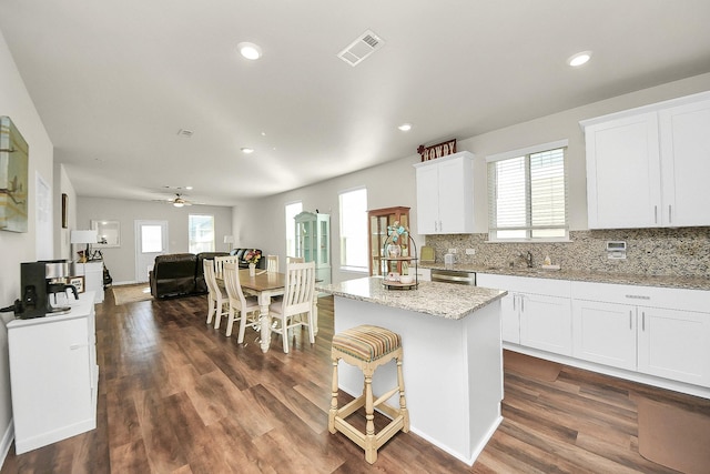 kitchen with a center island, dark wood-type flooring, white cabinets, ceiling fan, and light stone counters