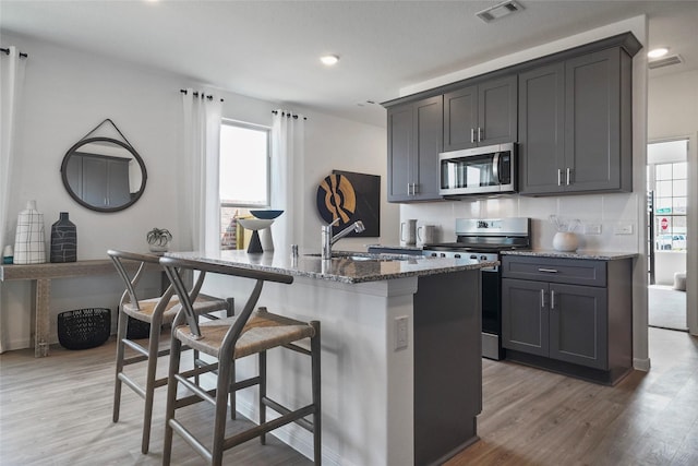 kitchen featuring appliances with stainless steel finishes, sink, a center island with sink, dark stone countertops, and hardwood / wood-style floors