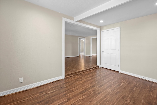 spare room with beam ceiling and dark hardwood / wood-style flooring