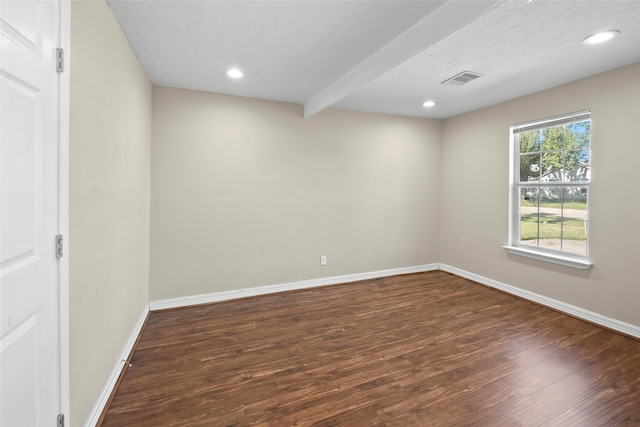 empty room featuring beam ceiling, dark wood-type flooring, and a textured ceiling