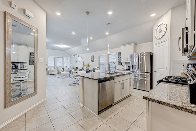 kitchen with white cabinetry, stainless steel appliances, sink, stone countertops, and a kitchen island with sink