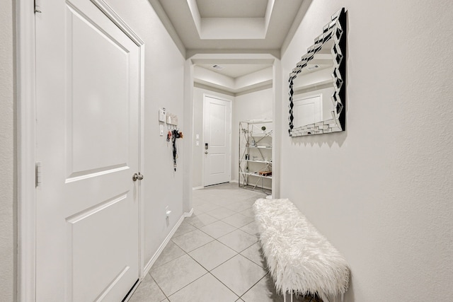 hallway featuring light tile patterned floors and a tray ceiling