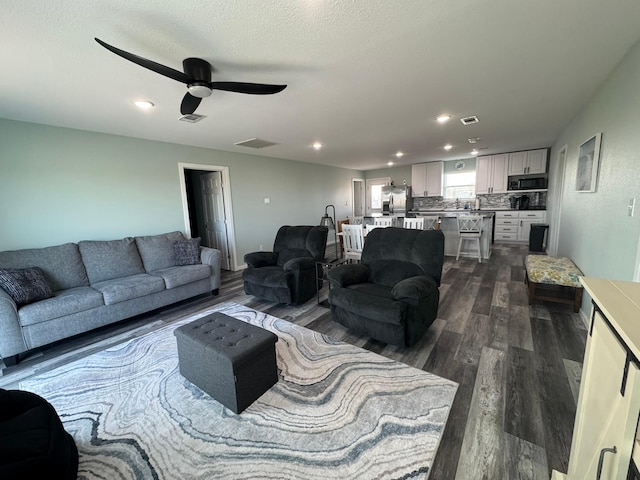 living room with dark wood-type flooring, ceiling fan, and a textured ceiling