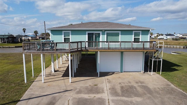 rear view of house featuring driveway, a garage, a lawn, roof with shingles, and a deck