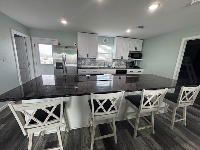 kitchen with black microwave, tasteful backsplash, dark wood-type flooring, and stainless steel fridge