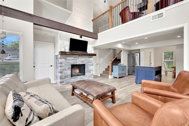 living room featuring a stone fireplace, a towering ceiling, and light hardwood / wood-style flooring