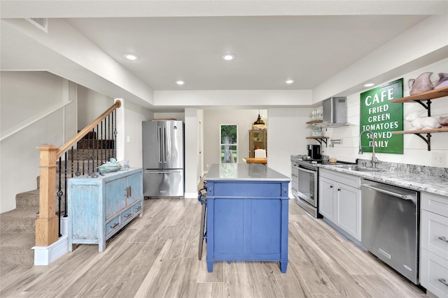 kitchen with appliances with stainless steel finishes, wall chimney exhaust hood, sink, a center island, and light hardwood / wood-style floors