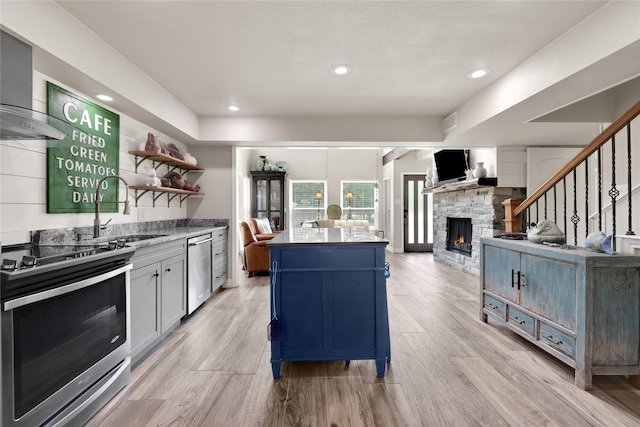 kitchen with a center island, wall chimney range hood, sink, a fireplace, and stainless steel appliances