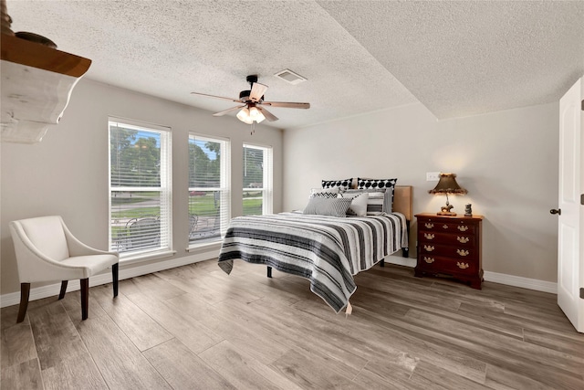 bedroom with ceiling fan, wood-type flooring, and a textured ceiling