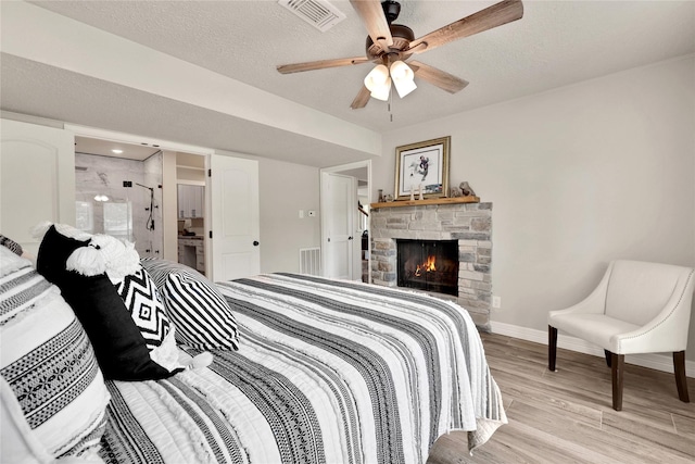 bedroom with ceiling fan, light hardwood / wood-style floors, a textured ceiling, and a fireplace