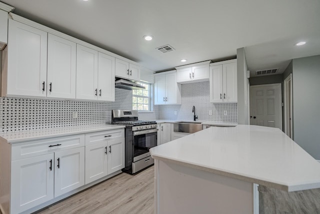 kitchen featuring sink, stainless steel gas stove, decorative backsplash, a kitchen island, and white cabinetry