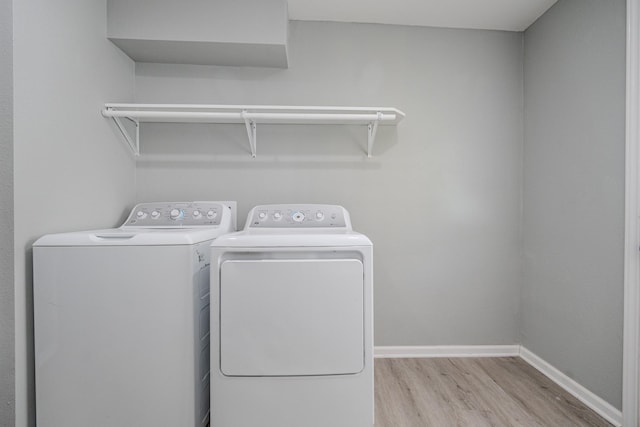 clothes washing area with washing machine and dryer and light wood-type flooring