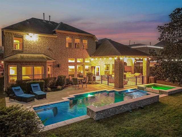 back house at dusk featuring a swimming pool with hot tub and a patio area