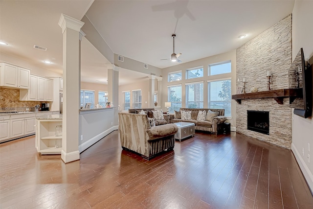 living room with a stone fireplace, ceiling fan, dark hardwood / wood-style flooring, and a healthy amount of sunlight