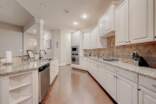 kitchen with appliances with stainless steel finishes, light stone counters, sink, light hardwood / wood-style flooring, and white cabinetry