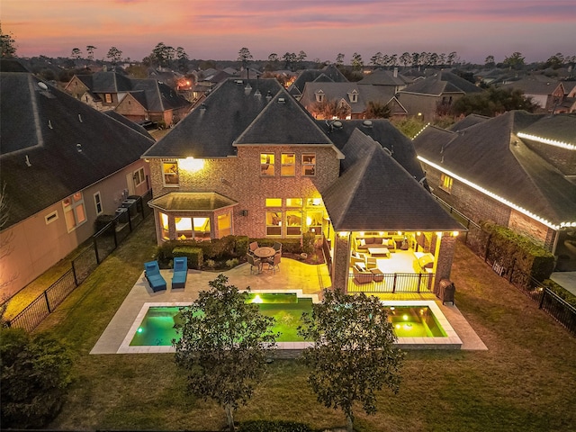 back house at dusk with a lawn, an outdoor living space, a fenced in pool, and a patio