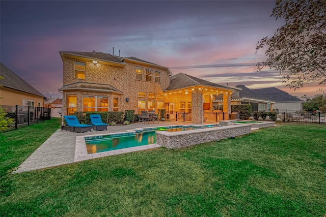 back house at dusk featuring a pool with hot tub, a yard, and a patio